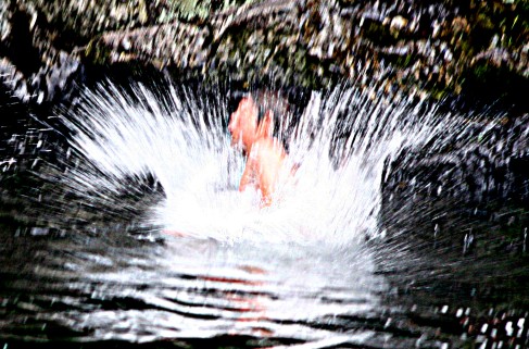 splash of water as child enters river by jumping in from rock above