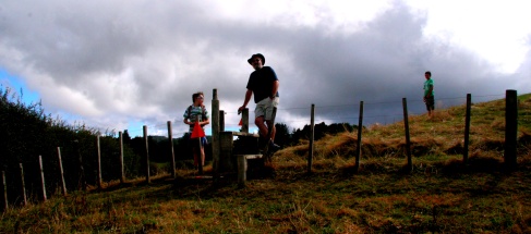 A man and a boy standing by a fence in a paddock on a hillside