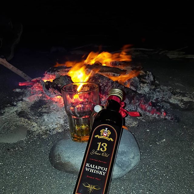 fire on the beach with a glass and a bottle of whisky in the foreground